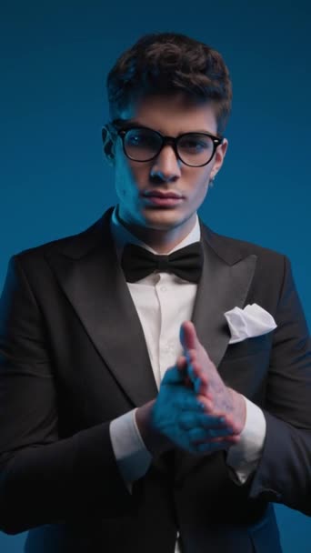 projekt video atraktivní mladý muž s brýlemi na sobě elegantní černý smoking tření dlaně a těšíme se na barevné pozadí - Záběry, video