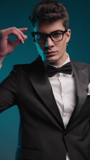 zblízka elegantní ženich v černém smokingu uspořádání jeho brýle při pohledu kolem na barvu měnící pozadí - Záběry, video