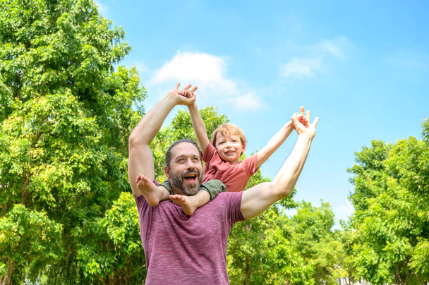 little boy play with dad on summer day. father carries his son on his shoulders in park. father day happy family child dream concept - Photo, Image