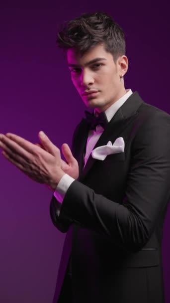 boční pohled na elegantní muž v černém smokingu tření dlaně a dělat gesto mlčení s prstem v přední barevné pozadí - Záběry, video