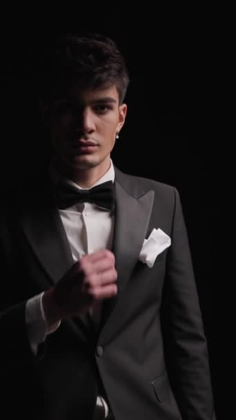 mysterious elegant businessman in black tuxedo adjusting black bowtie and tux, looking forward and walking away - Footage, Video