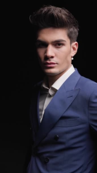 Projektvideo eines sexy jungen Geschäftsmannes, der die Hände in den Taschen hält und nach vorne blickt, während er einen blauen Anzug vor schwarzem Hintergrund trägt - Filmmaterial, Video