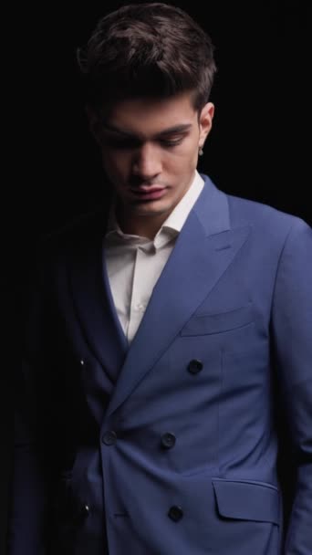 closeup of elegant fashion man wearing double breasted blue suit standing with hands in pockets on dark background - Footage, Video