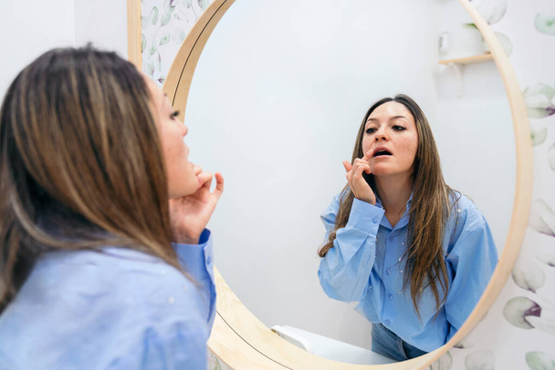 Dans un moment intime de soins de la peau, une femme applique soigneusement un produit de soin des lèvres, reflété dans un miroir dans une clinique professionnelle - Photo, image