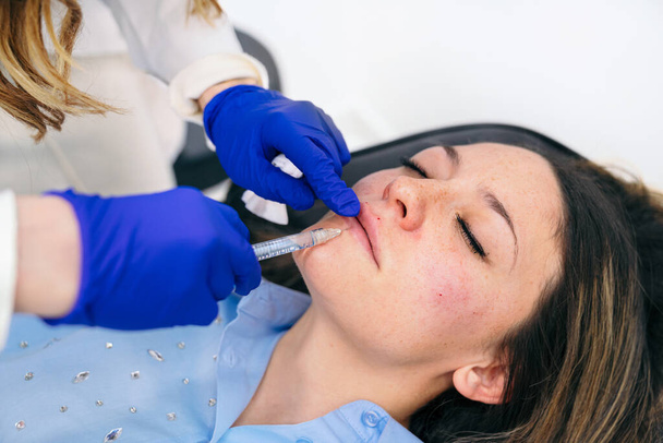 Focused aesthetician administers a hyaluronic acid injection into the lower lip for balanced, full lip augmentation. - Photo, Image