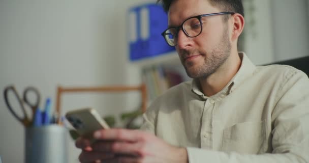 Uomo d'affari con gli occhiali e sms attraverso lo smart phone in ufficio - Filmati, video