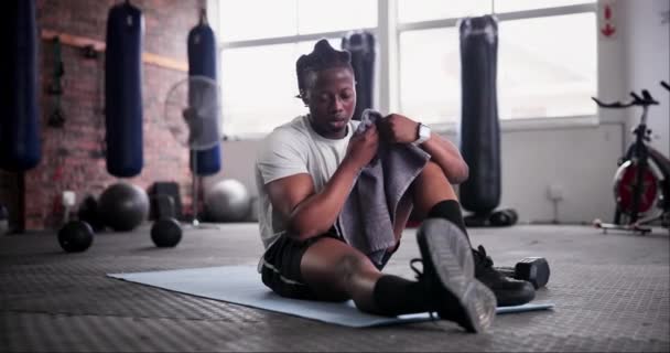 Fitness, tired and black man on floor with towel rest for bodybuilder training, exercise and gym workout. Sports, sweat and person with fatigue, relax and on break for wellness, health and recovery. - Footage, Video