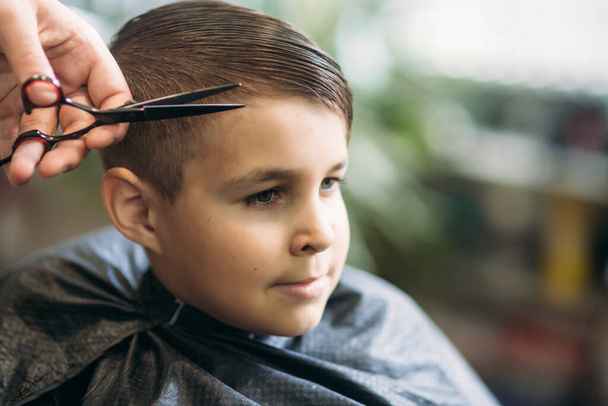 Chłopak coraz fryzura przez nożyczek w fryzjera. Fryzjer użyć nożyczek. - Zdjęcie, obraz