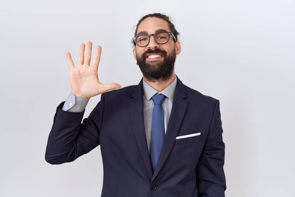 Hispanic man with beard wearing suit and tie showing and pointing up with fingers number five while smiling confident and happy.  - Foto, immagini