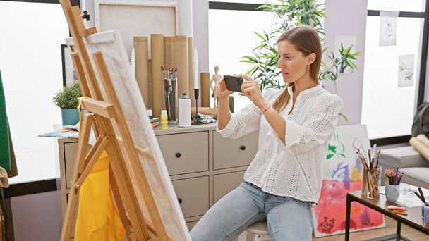 Uma jovem mulher captura sua arte com uma câmera em um estúdio de arte brilhantemente iluminado. - Foto, Imagem