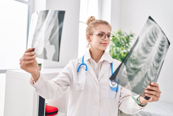 Jeune femme blonde médecin à la recherche de rayons X debout à la clinique - Photo, image