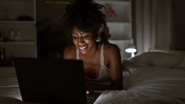 Afroamerikanerin trägt Dessous mit Laptop im Schlafzimmer - Foto, Bild