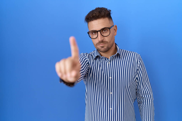 Homme hispanique à la barbe portant des lunettes pointant le doigt vers le haut et l'expression en colère, ne montrant aucun geste  - Photo, image