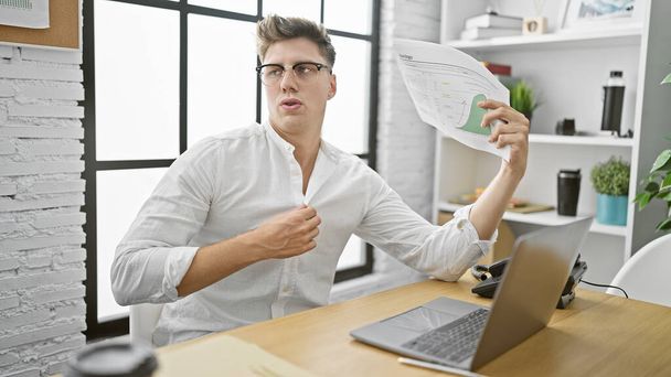 Young caucasian man suffering from hot air in office, hardworking employee struggles with heat while making business documents - Photo, Image