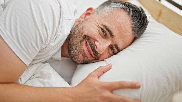 ベッドルームのベッドに横たわって自信を持って微笑む灰色の髪の男 - 写真・画像