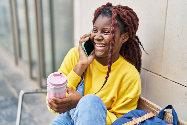 Afrika kökenli Amerikalı kız öğrenci akıllı telefondan konuşuyor üniversitede kahve içiyor. - Fotoğraf, Görsel