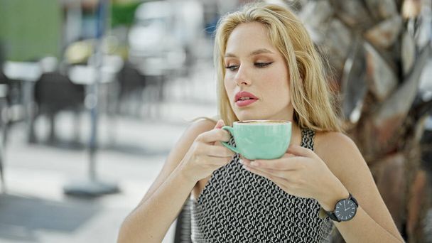 Jonge blonde vrouw met kopje koffie op tafel op het terras van de coffeeshop - Foto, afbeelding