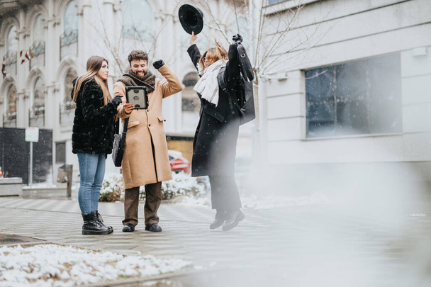 Les jeunes à la mode hivernale s'engagent dans une réunion décontractée en plein air avec une tablette lors d'une journée urbaine enneigée, respirant le travail d'équipe et la flexibilité. - Photo, image
