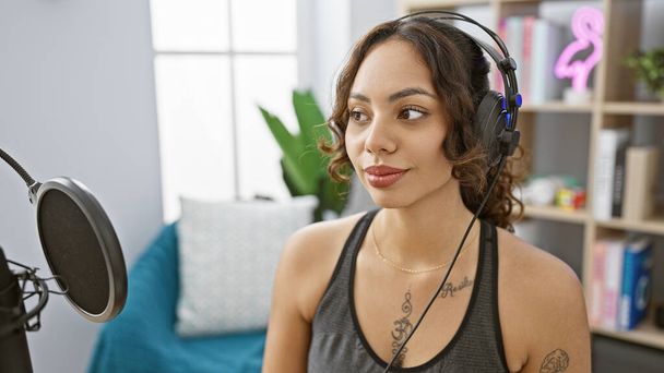 Молода жінка з навушниками в домашньому середовищі студії, випромінюючи розслаблену креативність. - Фото, зображення
