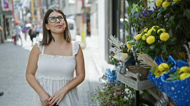 Charming hispanic woman in glasses standing amongst tokyo's urban floral beauty - Photo, Image