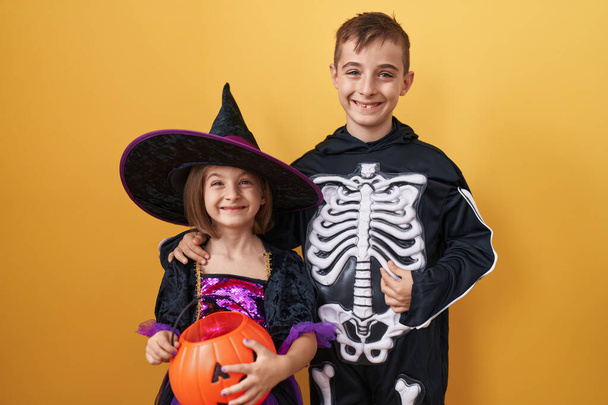 Verrukte broer en zus dragen halloween kostuums, delen tandenpoets, zelfverzekerde glimlachen over een geïsoleerde gele achtergrond. belichamen vreugde, geluk en een positieve kijk samen. - Foto, afbeelding
