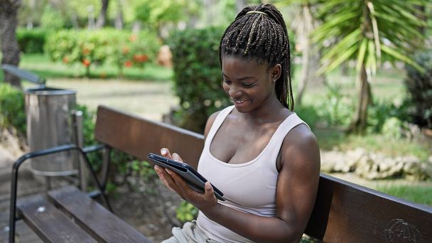 Africano americano mulher usando touchpad sentado no banco no parque - Foto, Imagem