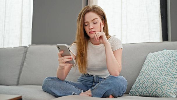 Young blonde woman using smartphone looking upset at home - Photo, Image