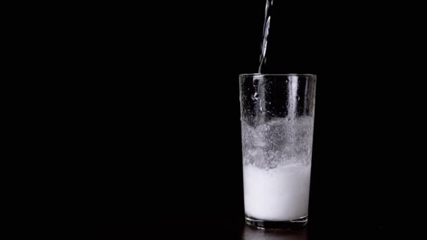 Chemische Reaktion von Soda und Essig in einem Glasbecher auf schwarzem Hintergrund. Textur. Flüssigkeit wird mit der Mischung in ein Glas gegossen. Bildung von Kohlendioxid, Schaum, Blasen. Chemische Experimente. - Filmmaterial, Video