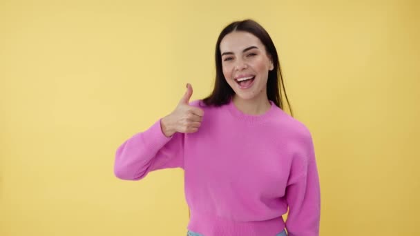 Viehättävä brunette nainen positiivinen hymy osoittaa peukalo ylös ele poseeratessaan yli keltainen studio tausta. Valkoihoinen nuori nainen vaaleanpunainen pusero antaa vilpittömiä suosituksia ja neuvoja. - Materiaali, video