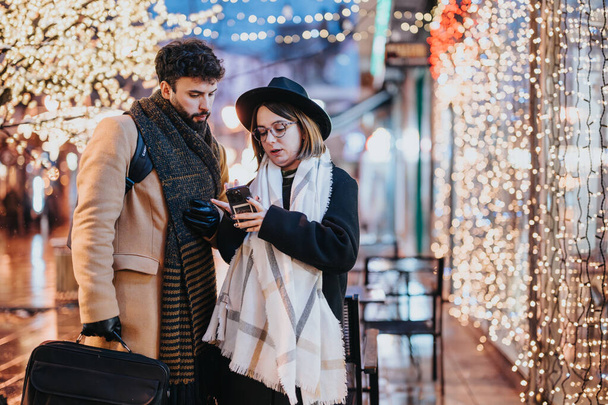 Zwei junge Erwachsene mit Smartphone unter festlicher Stadtbeleuchtung. - Foto, Bild