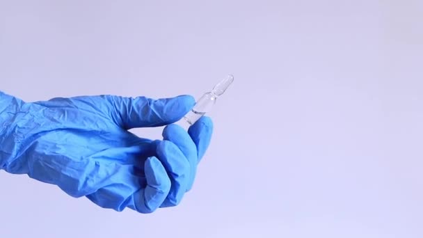 A nő keze egy kék orvosi kesztyűben egy gyógyszeres üvegampullát tart. Üvegampullák antibiotikumokkal vagy vakcinával, könnyű háttérrel. Egy orvos vagy nővér egy gyógyszert tart a kezében. - Felvétel, videó