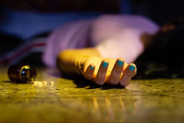 Indyjska lub azjatycka martwa kobieta z wyciągniętą ręką i tabletkami nasennymi leżącymi na podłodze w koncepcji samobójstwa w ciemnym pokoju. - Zdjęcie, obraz
