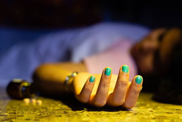 Ένα νεκρό σώμα Ινδιάνας ή Ασιάτισσας με απλωμένο χέρι και υπνωτικά χάπια ξαπλωμένα στο πάτωμα σε μια σκοτεινή έννοια αυτοκτονίας δωματίου. - Φωτογραφία, εικόνα