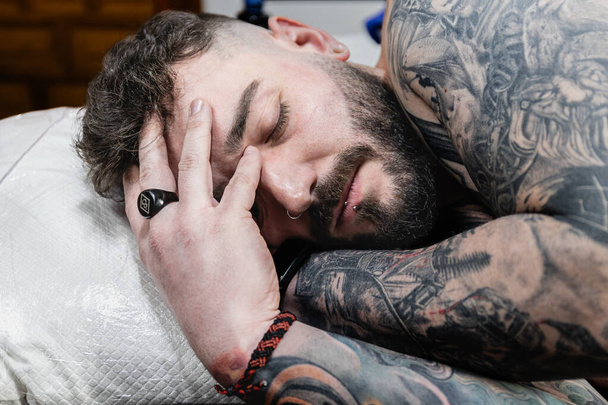 タトゥーに覆われた男性の横の写真は,休息するのに少し時間がかかります, 彼の手は穏やかに彼の頭をひっかける, 入るの忍耐と耐久性を体現しています. コンセプトビジネス,アート. - 写真・画像