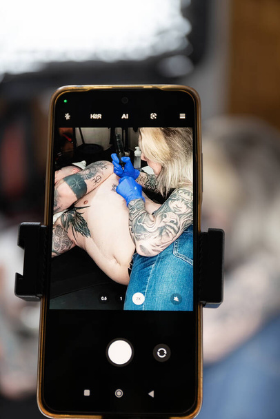 Vertikální fotografie detailní záběr obrazovky smartphonu zobrazující tetovaného umělce při práci, se zaměřením na umění a dovednosti. Kopírovat prostor.Koncepce obchodu, umění. - Fotografie, Obrázek