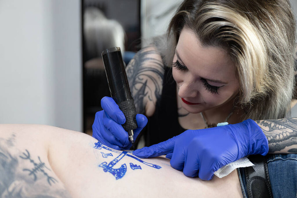 Горизонтальна фотографія Інтенсивний фокус як художник татуювання татуювання герба на тілі клієнта, втілюючи дизайн в життя. Концептуальний бізнес, мистецтво. - Фото, зображення