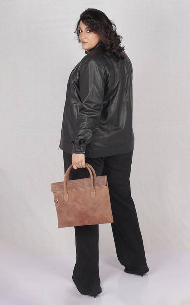 a woman in a black jacket and black pants holding a brown bag - Photo, image