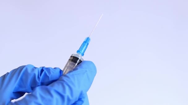 De hand van een vrouw in een blauwe medische handschoen houdt een spuit vast. Verpleegkundige of arts met een spuit van 2 ml. Vaccinatie. Injectie - Video