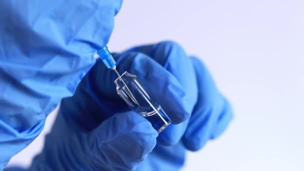 Een hand in een blauwe handschoen vult een spuit uit een ampul. Verpleegkundige of arts met een spuit van 2 ml. Vaccinatie. Injectie - Video