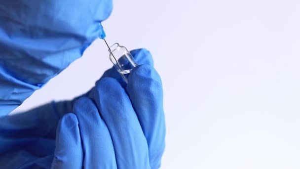 Een hand in een blauwe handschoen vult een spuit uit een ampul. Verpleegkundige of arts met een spuit van 2 ml. Vaccinatie. Injectie - Video