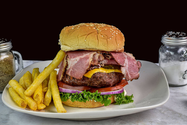 гамбургер с сыром из пастрами с помидорами и луком, подаваемый с картошкой фри, - Фото, изображение