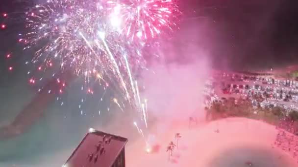 夜に爆発するカラフルな輝く花火の上を飛行するドローン. ワイキキリゾートで空で花火が爆発した. ハワイのオアフ島に観光客が集まっています. 夏休みで人生を祝う人 - 映像、動画