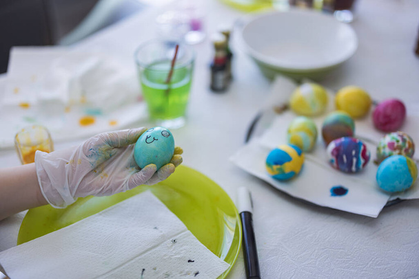 Vista de cerca de la mano del niño en guante de nitrilo desechable sosteniendo un huevo pintado en las tradiciones de Pascua. Países Bajos. - Foto, imagen