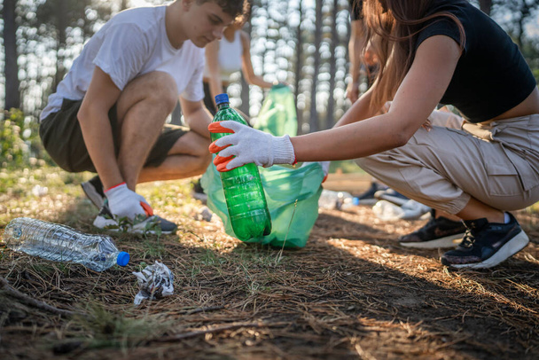Bir grup genç arkadaş Z erkek ve beyaz kadın atık plastik şişeleri ve kağıtları toplayarak güneşli bir günde çevre koruma kavramının doğasını temizliyorlar. - Fotoğraf, Görsel