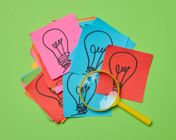 Lâmpadas desenhadas em folhas de papel e uma lupa de plástico, o conceito de busca de novas ideias. - Foto, Imagem