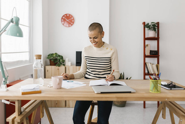 Pozitivní středně dospělá podnikatelka pracující z domácí kanceláře. Úspěšné podnikatelky píšou na notebook, který sedí na pracovišti - Fotografie, Obrázek