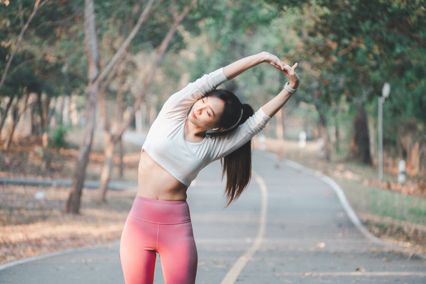 Concepto de carrera, mujer joven en forma realizando un ejercicio de estiramiento lateral en un sendero tranquilo parque rodeado de árboles - Foto, imagen