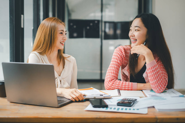 Conceito de análise de equipe de negócios, duas mulheres de negócios sorrindo e discutindo o trabalho com um laptop, calculadora e documentos em uma mesa de madeira - Foto, Imagem