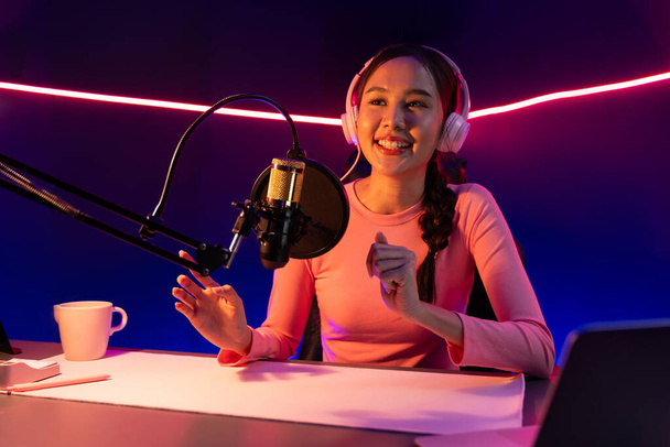 Hymyilevä luova nuori kaunis aasialainen vaikuttaja puhuu kanava positiivinen podcast puheen yöllä, käyttäen kannettavaa tietokonetta esitykseen verkossa vaaleanpunainen neon valo moderni studio. Stratagem. - Valokuva, kuva