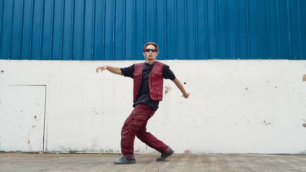 Jóképű utcai táncos, aki szünettáncot gyakorol a fehér hátsókertben. Sport férfi visel hip-hop stílusban, miközben mozog léptek a zene az utcán a kék háttér. Kültéri sport 2024. Hatálybalépés. - Fotó, kép